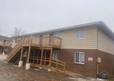 Exterior view of a residential building featuring a custom-built wooden deck with stair access and an adjacent accessibility ramp, showcasing durable construction designed for safety and outdoor living enhancement.