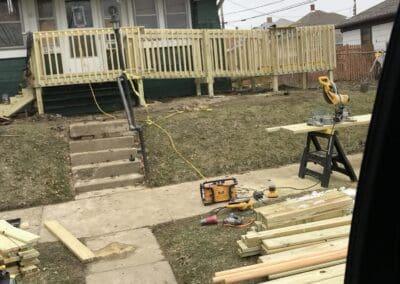Construction site showing a wooden deck and ramp in progress attached to a house, with tools and lumber scattered on the ground, illustrating custom outdoor deck and ramp building for accessibility and outdoor living improvements.