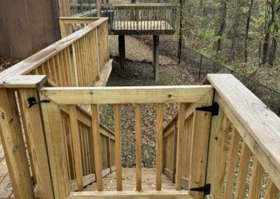Wooden outdoor deck with safety railing and gate, surrounded by trees, showcasing durable craftsmanship ideal for walkways, ramps, and backyard entertaining spaces.